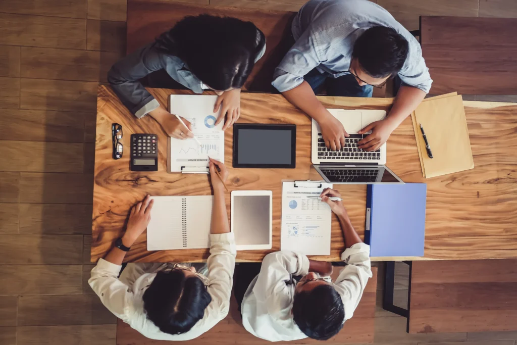Top-down view of professionals working on reports and graphs, analyzing project management certification options.