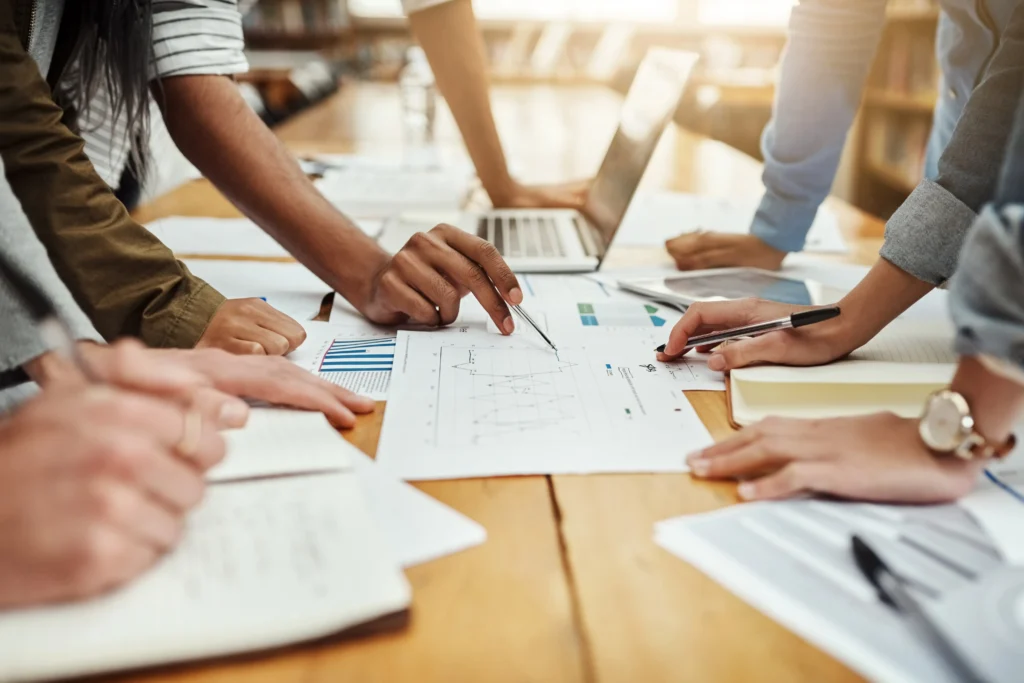Team of professionals collaborating over printed charts and a laptop, evaluating various PMP online course options.