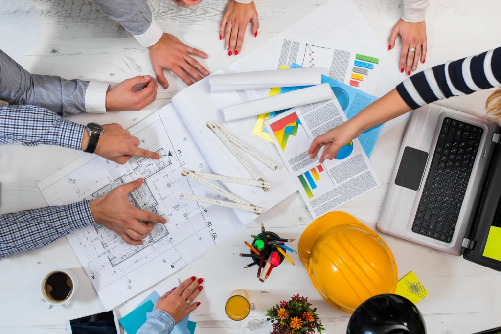 Team collaborating over architectural plans and PMP exam change documents on a table