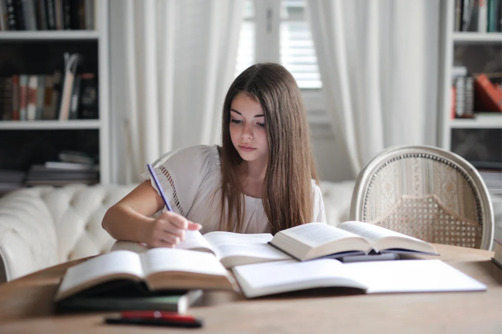 Young woman deeply focused on PMP exam preparation books in a cozy home study environment.