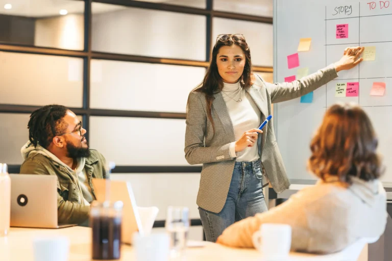 A project manager explaining PMP exam pattern updates on a whiteboard during a team meeting.